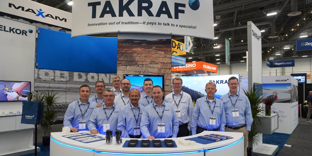Eleven men standing behind a TAKRAF booth