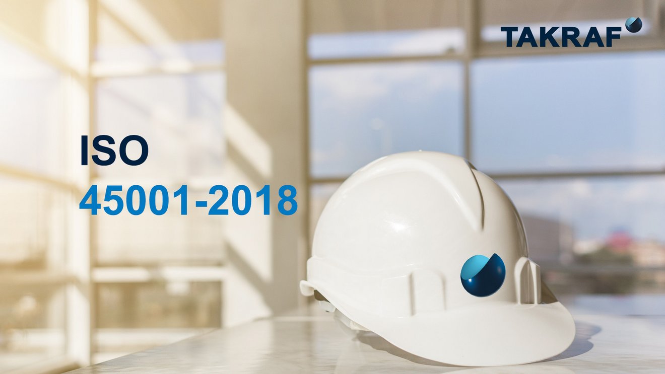 White safety helmet with the TAKRAF logo on a table, writing ISO 45001 - 2018 in front