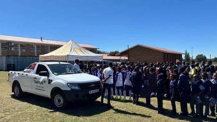 The picture shows the soccer teams waiting to register in front of a pavilion on the football field. Next to it a TAKRAF jeep.