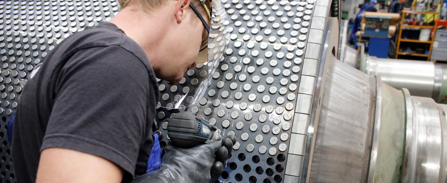 A production worker is refurbishing a High Pressure Grinding Roll.