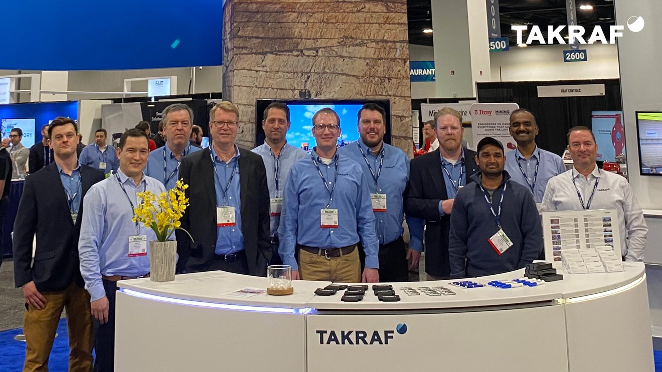 The TAKRAF Group team standing behind a booth with the TAKRAF Logo