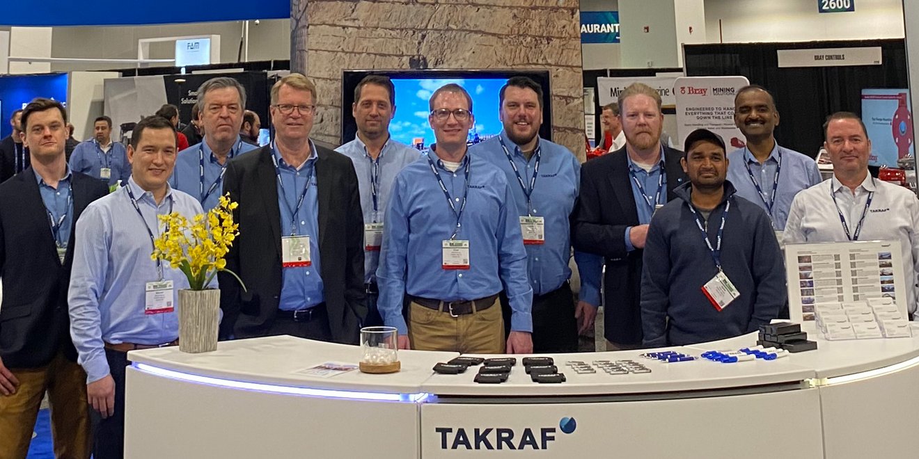 The TAKRAF Group team standing behind a booth with the TAKRAF Logo