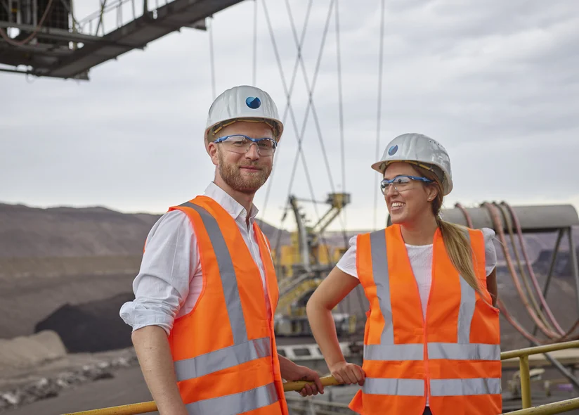 Two engineers wearing hard hats and high-visibility vests, looking out over the open-pit mine