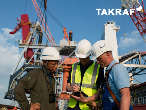 Three people (male) infront of a shiploader looking into a document