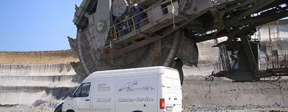 A TAKRAF service van stands on the construction site in front of a bucket wheel excavator for maintenance.
