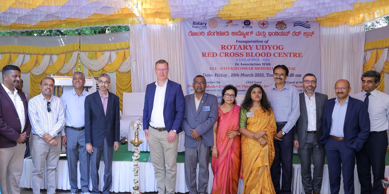 A group of people, including TAKRAF and DELKOR representatives, Rotary Udyog and Red Cross members, standing in front of a banner reading ‘Rotary Udyog Red Cross Blood Centre