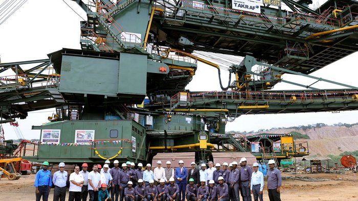KING CHERA BWE 1573 machine at NLCIL, India MINE II after a major revamp. A group of peaople are standing infront of a hudge bucket-wheel excavater in an Indian mine.