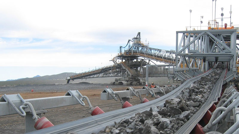 multiple long conveyor belts and steel support structures winding across a rugged mining landscape, illustrating TAKRAF’s large-scale materials handling system in operation